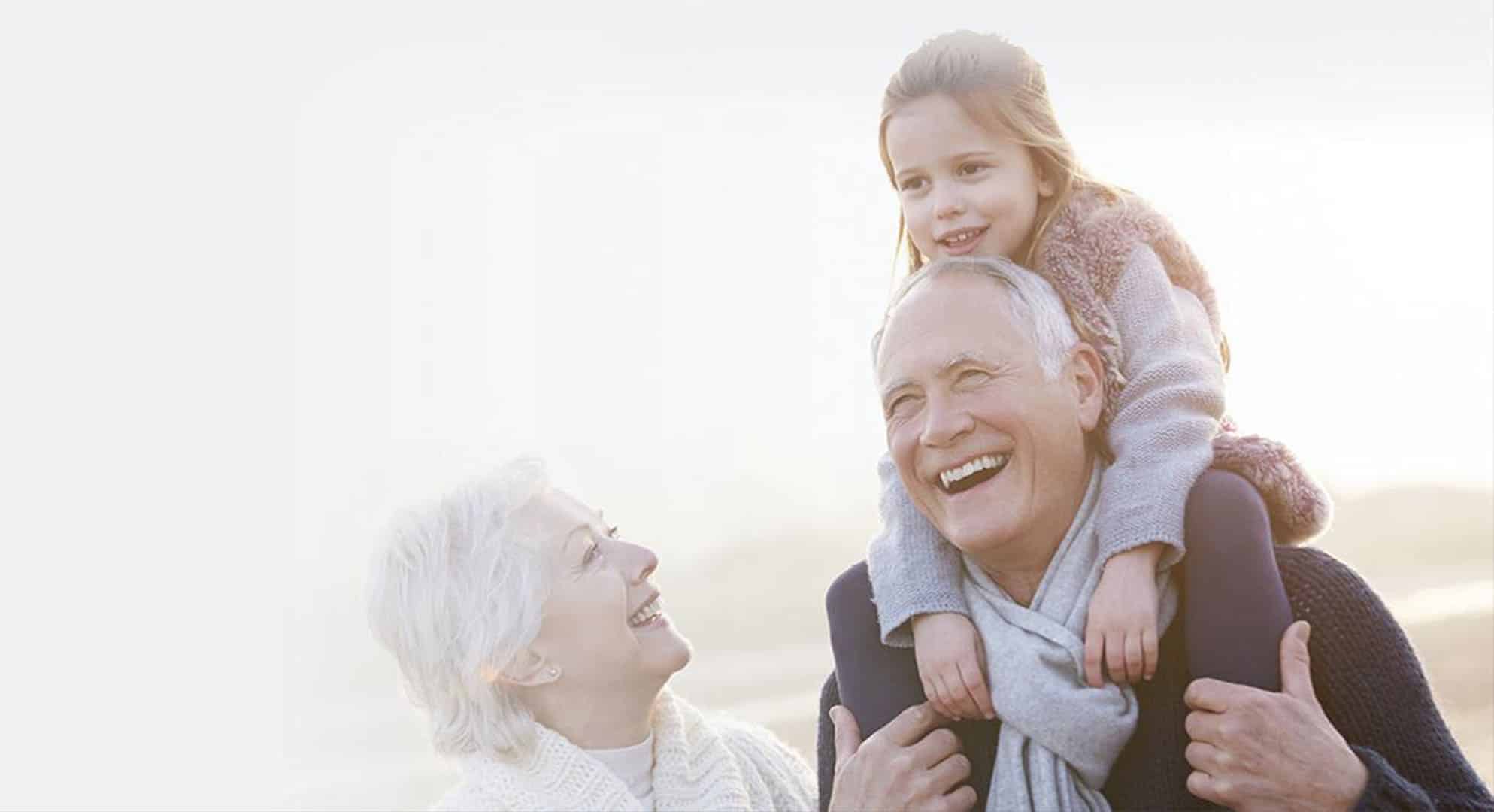 Girl smiling, riding on grandpa's shoulders with grandma watching and smiling